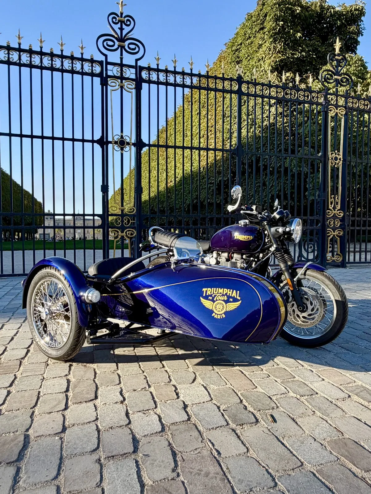 Side-car Triumph bleu du Royal Escape devant des grilles royales dorées