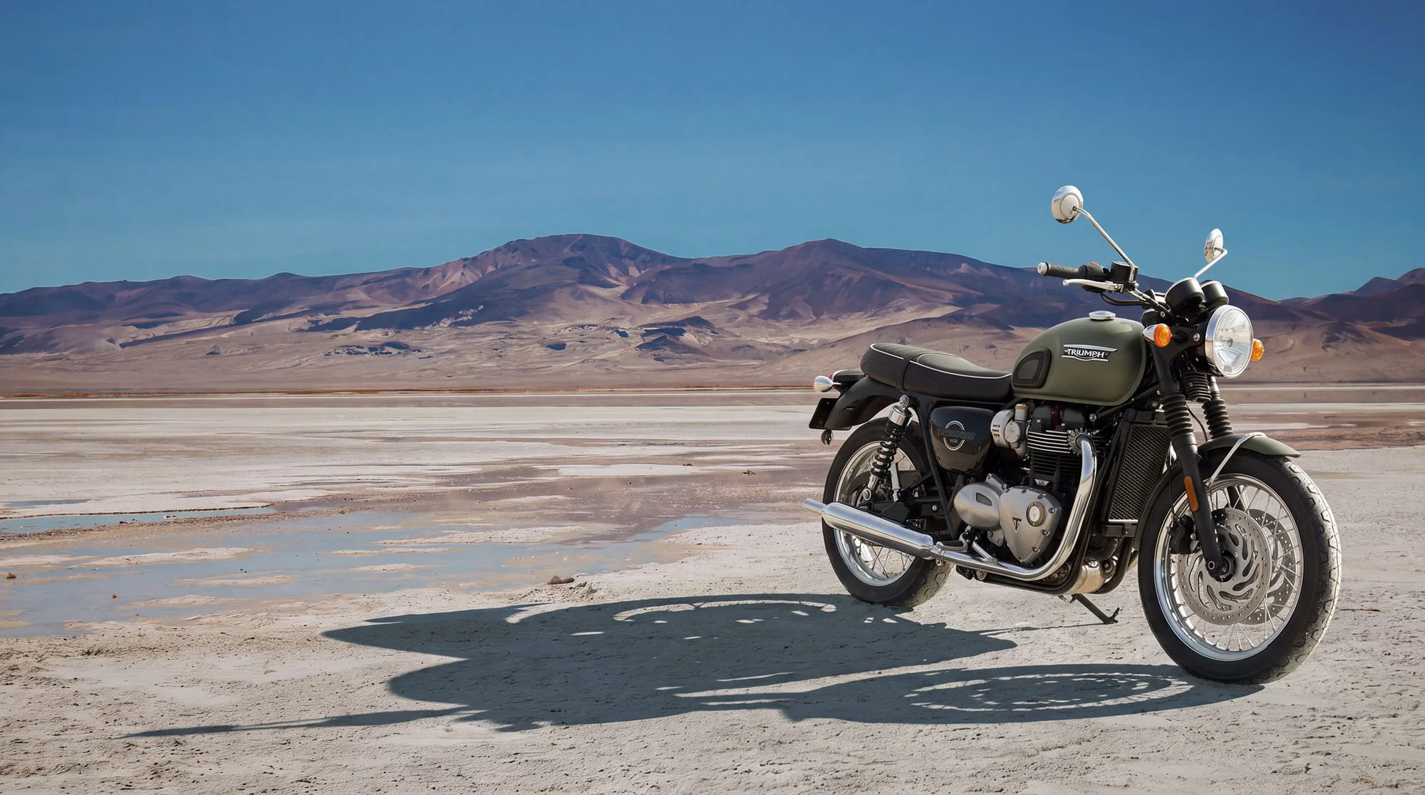 Triumph Bonneville T120 verte posée sur un lac salé face aux montagnes