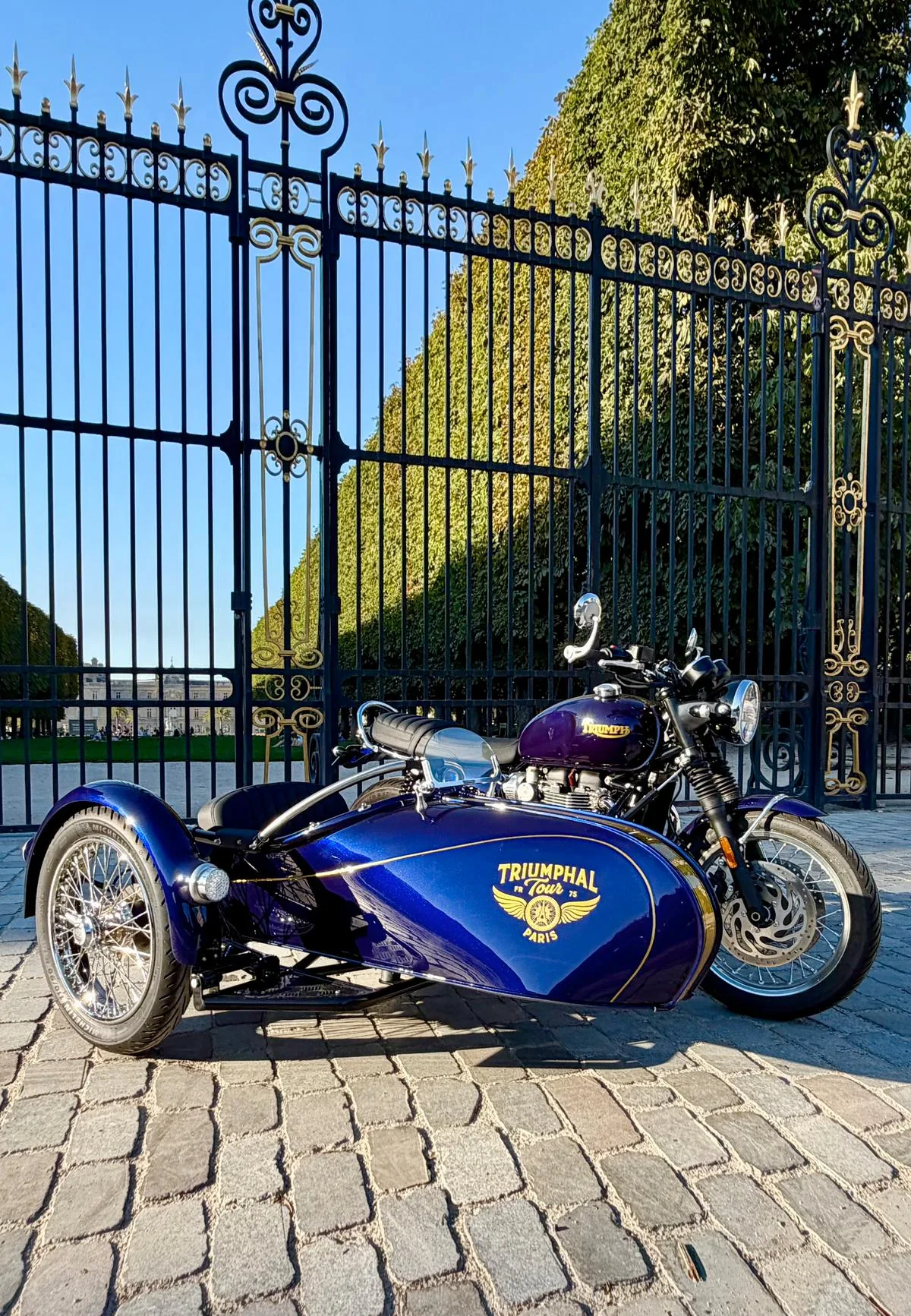 Side-car Triumph bleu du Royal Escape devant des grilles royales dorées